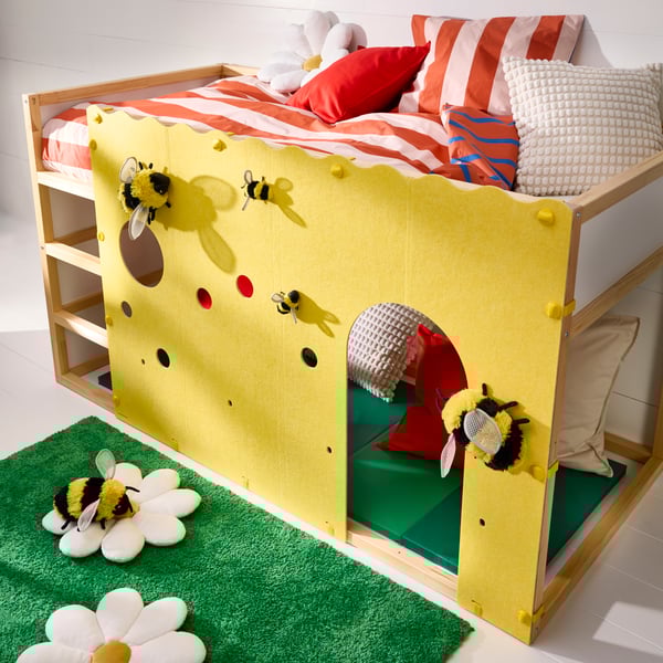 A KURA bed accessory in yellow with cut-outs and decorative elements attached to a KURA reversible bed in a child’s room.