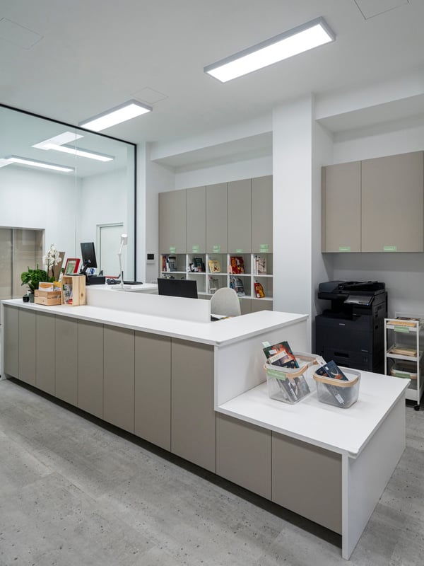 La reception della Biblioteca comunale di Brescia Roncadelle, composta da mobili METOD con piani di lavoro su misura JÄRSTORP e scrivanie MITTZON. Sul bancone ci sono diversi materiali informativi e fogli e un cestino RISATORP.