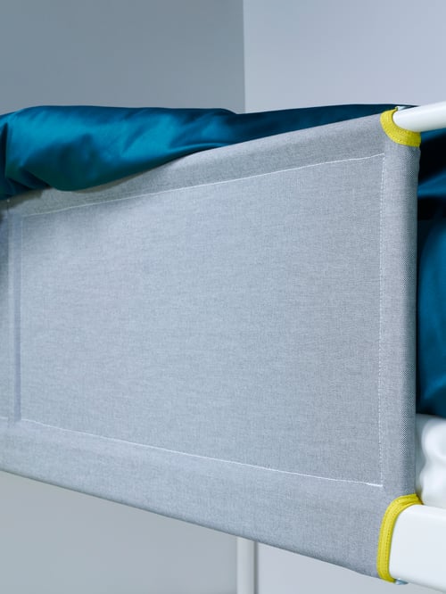 Prim-plan cu bara de protecție îmbrăcată cu material textil a unui pat suprapus.