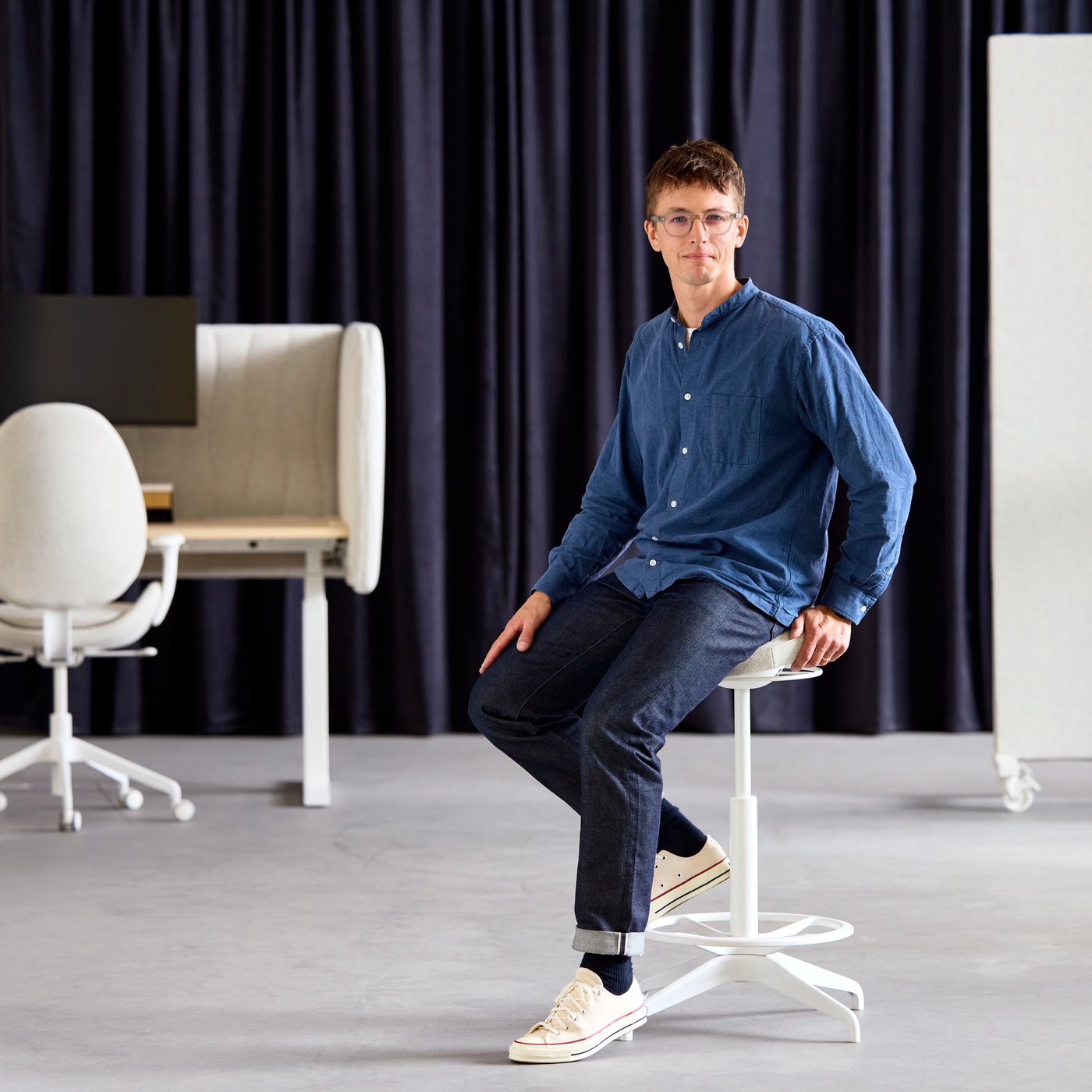 Philip Dilé, product developer, sits on a beige LIDKULLEN active sit/stand support, with a sit/stand desk in the background.