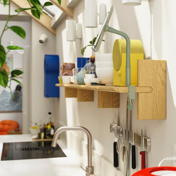A KLAVRESTRÖM wall shelf, made of solid oak, is mounted on a kitchen wall and a NATTBAD Bluetooth speaker is placed on it.