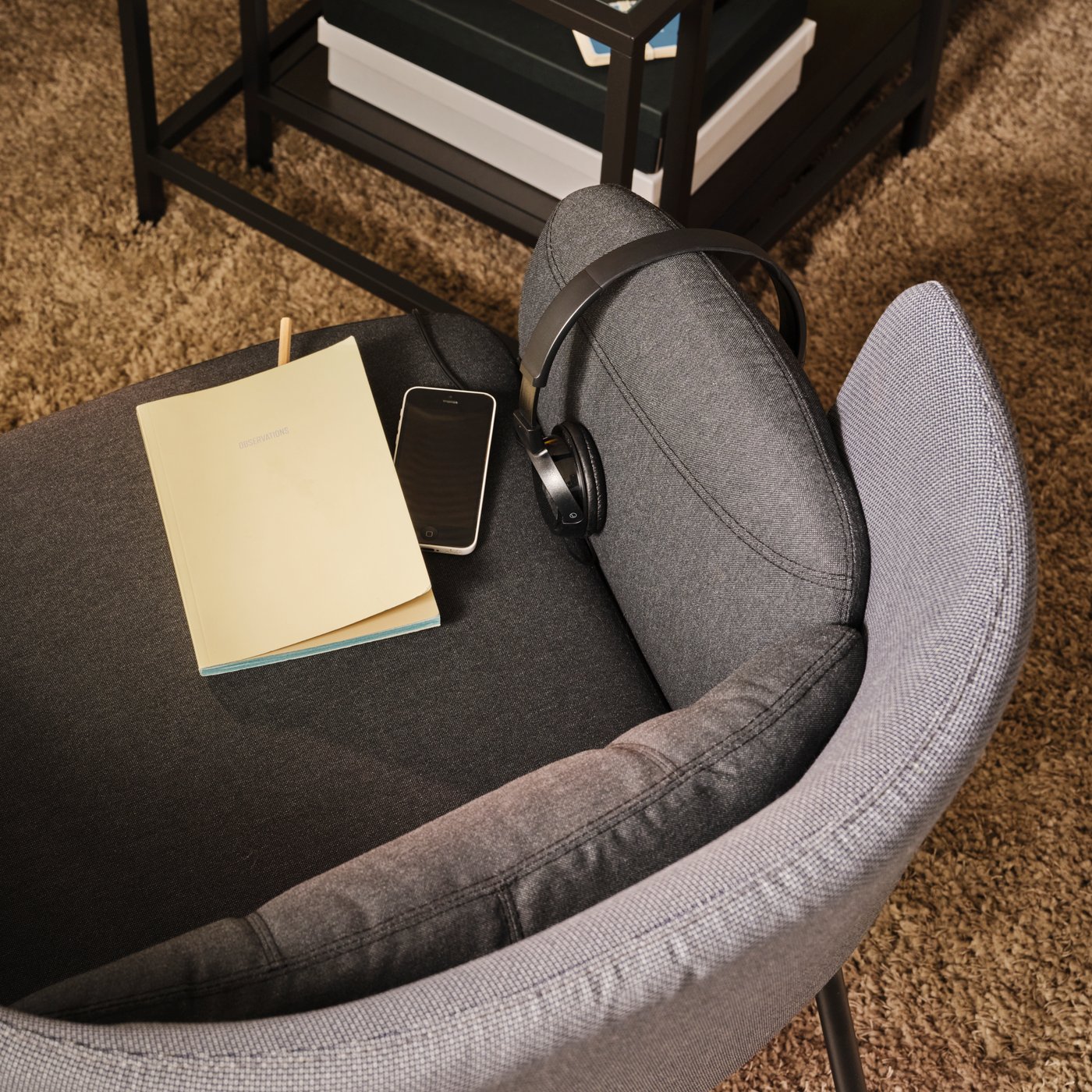A dark-grey BINGSTA armchair holding a phone, headphones and a notepad, and standing by a VITTSJÖ nest of tables.