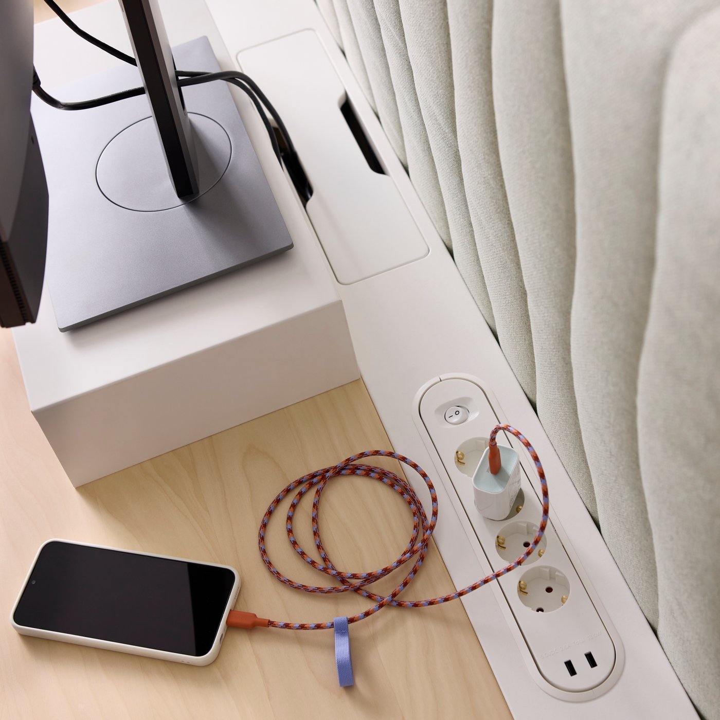 Närbild på en beige MITTZON akustisk skrivbordsskärm i Gunnared beige, med en smartphone och prydligt hanterade laddningskablar.