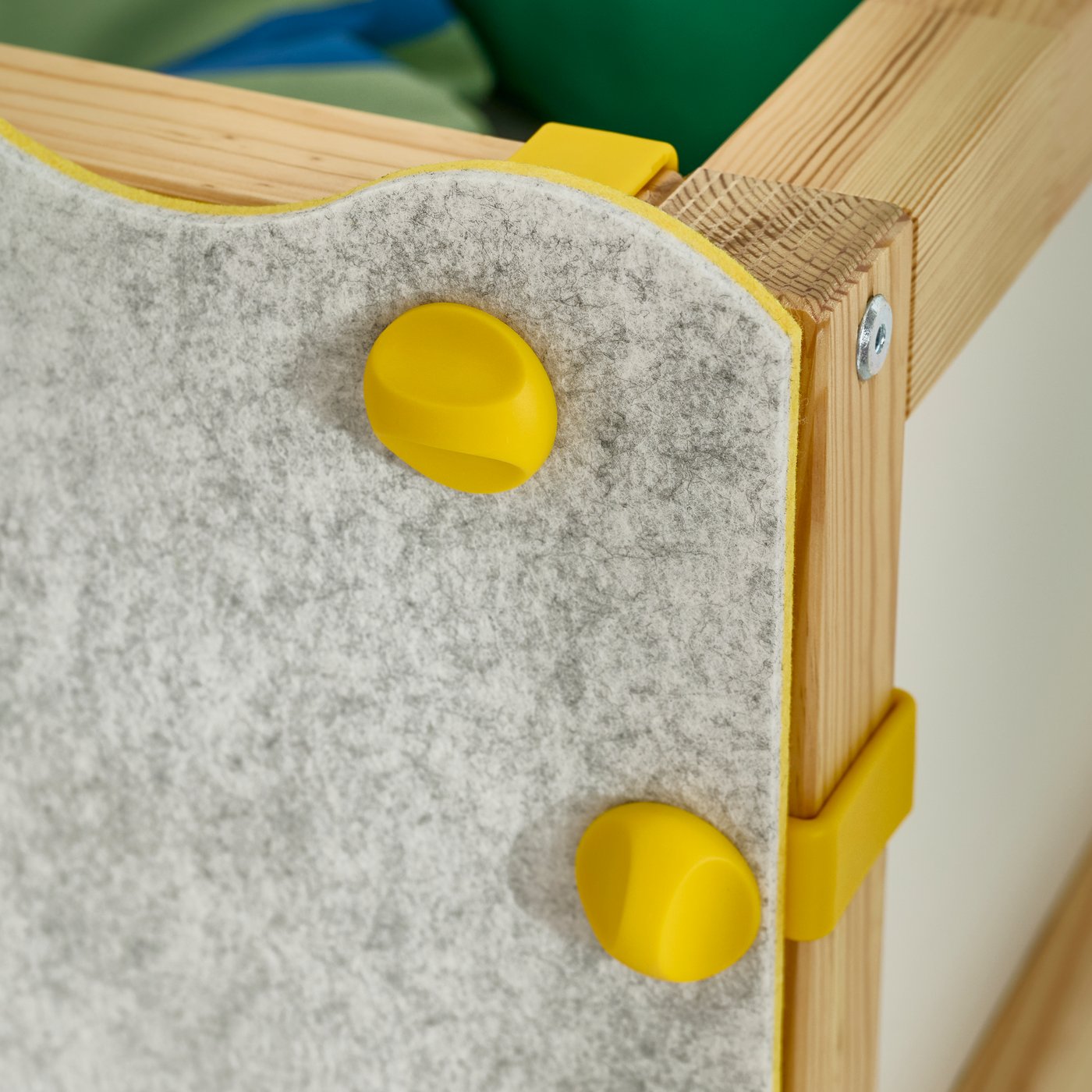 A KURA bed accessory felt panel secured to the KURA reversible bed using yellow fastening knobs.