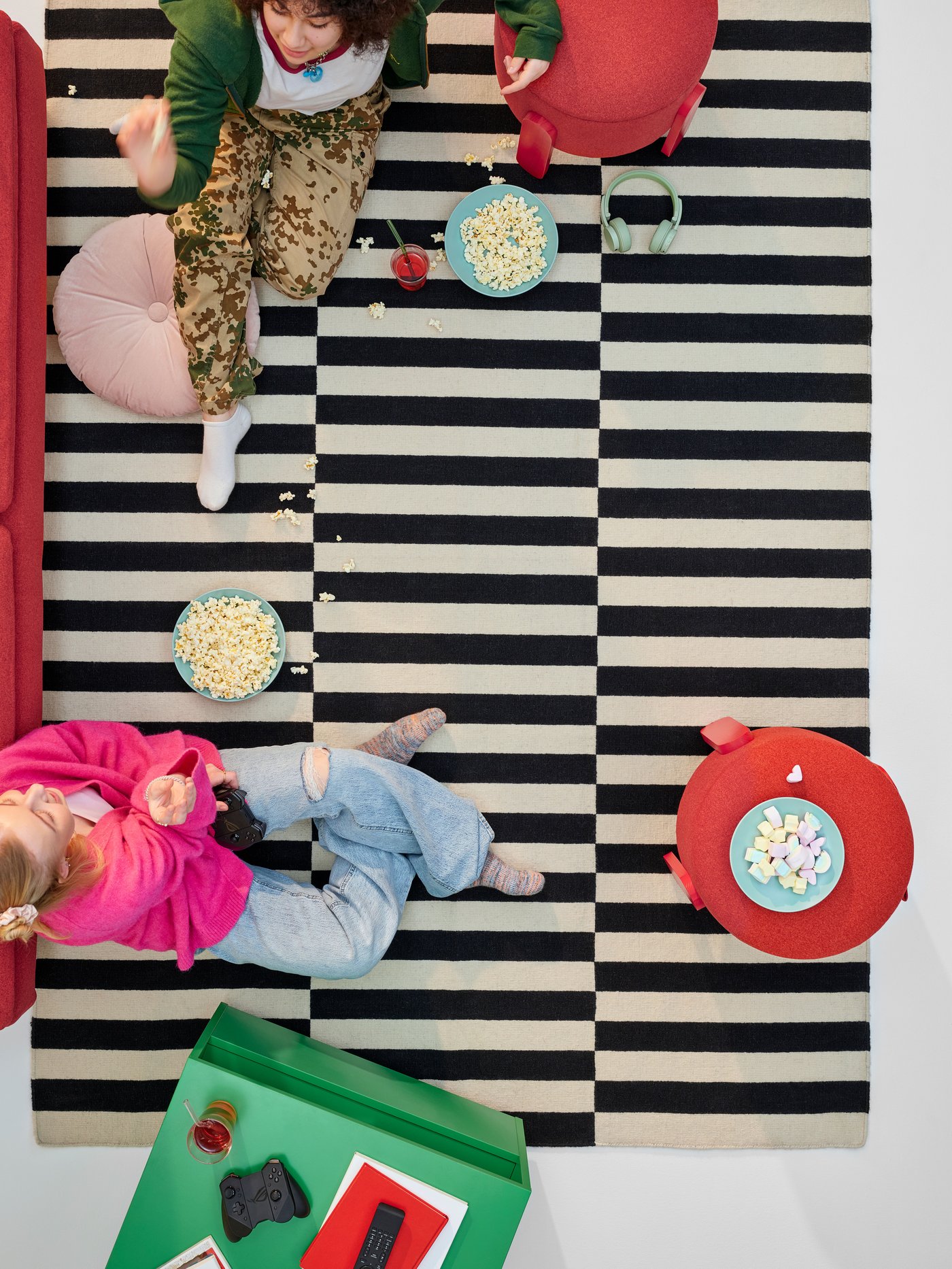 En fågelperspektivvy av två tonåringar som umgås och äter snacks på en svartvit randig STOCKHOLM ullmatta.