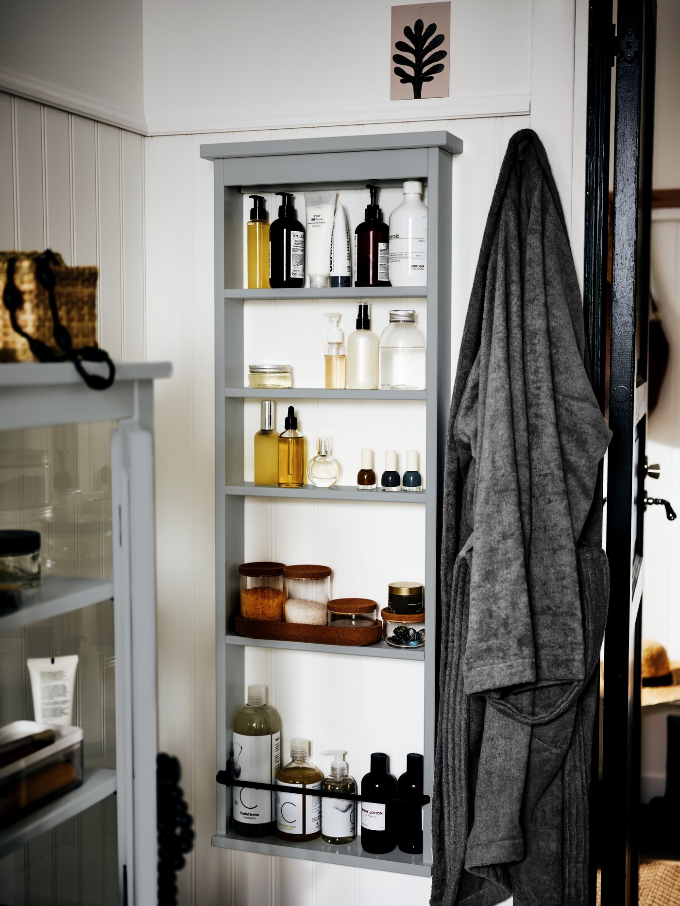 The corner of a white bathroom with a HEMNES wall shelf on one wall. Toiletries and bathroom accessories are on the shelves.