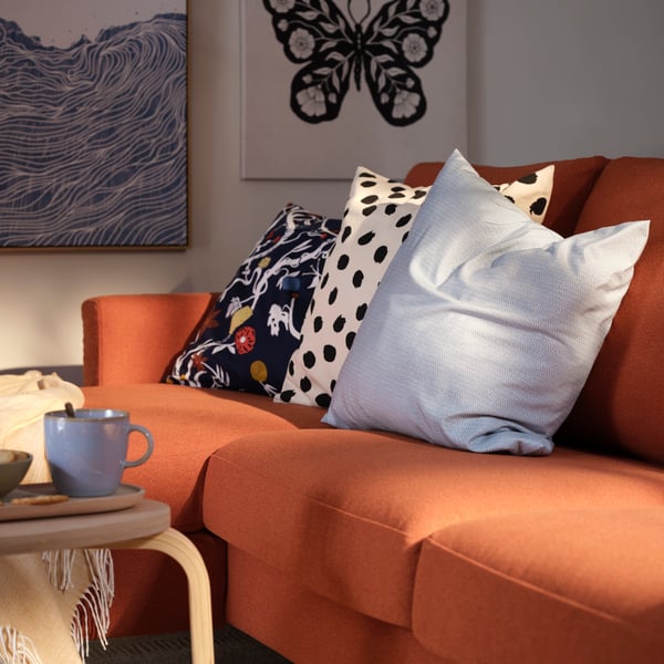 A living room with a red-brown SALTSJÖBADEN three-seat sofa with chaise longue, complemented by decorative cushions.
