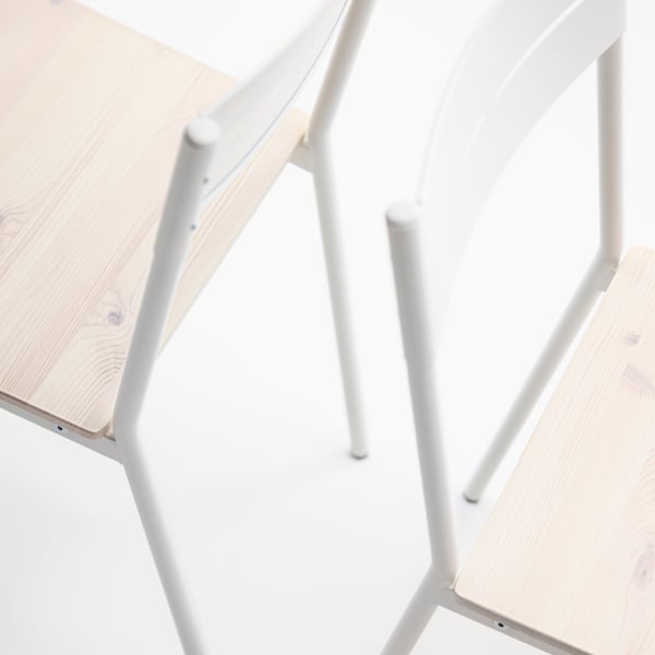 Close-up of two BUSLÄTT dining chairs, with sleek white metal frames and seats in solid pine wood.