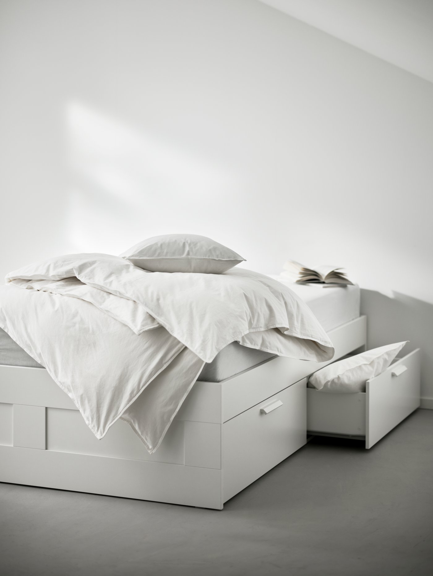 Detalle de una estructura de cama blanca de madera con almacenaje formado por 4 cajones grandes debajo.