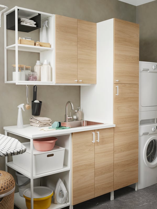 A utility area with an ENHET laundry set-up in white oak with a washing machine and a KUGGIS box with lid in white.