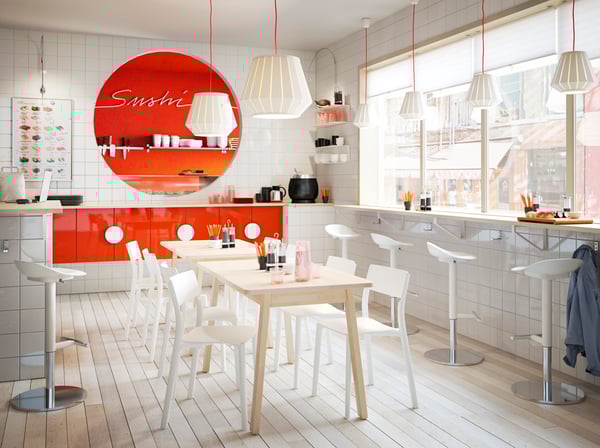 Urządzona na biało restauracja sushi z pomarańczowymi akcentami oraz białymi stołkami barowymi i krzesłami JANINGE.