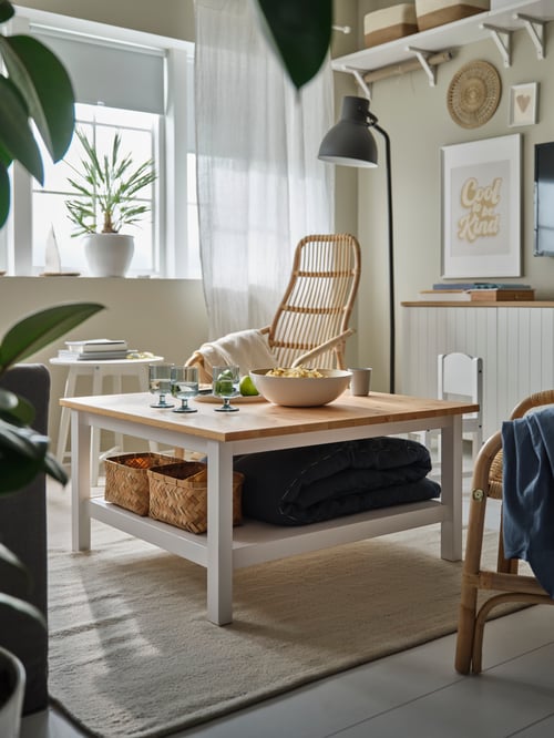 A square HEMNES coffee table with two tiers is on a flatwoven TIDTABELL rug, with a SALNÖ chair and a lamp in the background