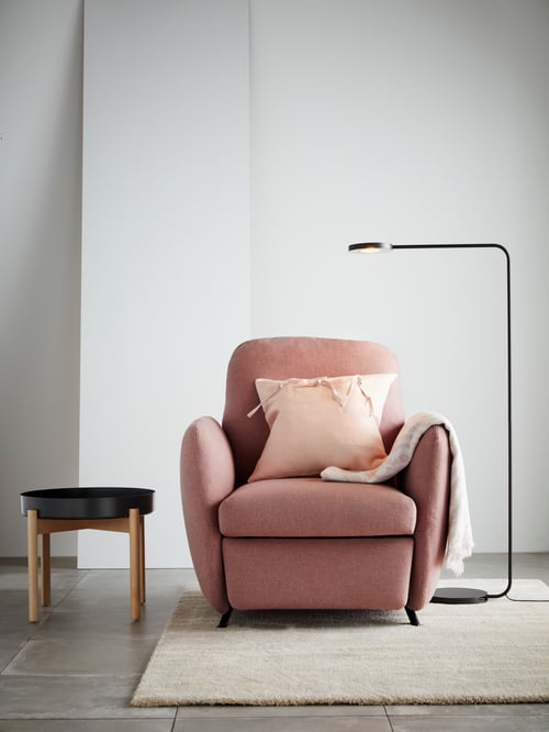 White room with white rug, pink recliner, pink cushion, black LED floor lamp and black coffee table with wooden legs.
