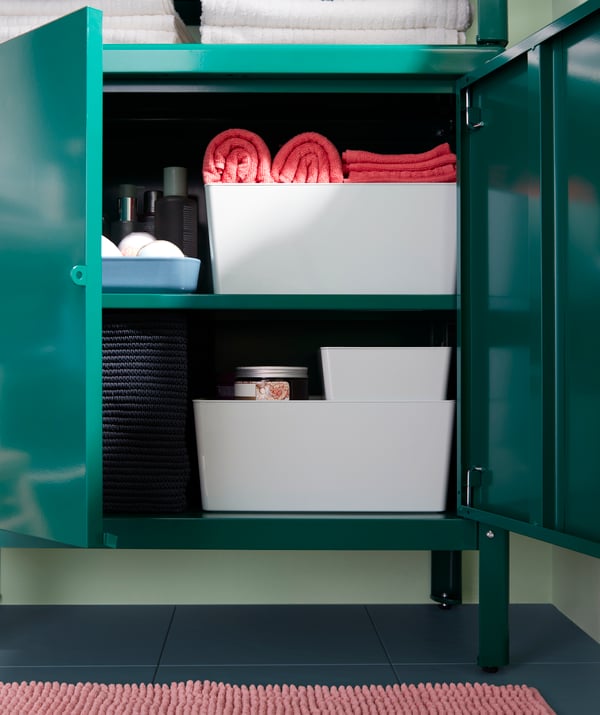 Ein grüner Metallschrank mit geöffneten Türen, u. a. mit einer KUGGIS Box mit Deckel und einem NORDRANA Korb in Blau