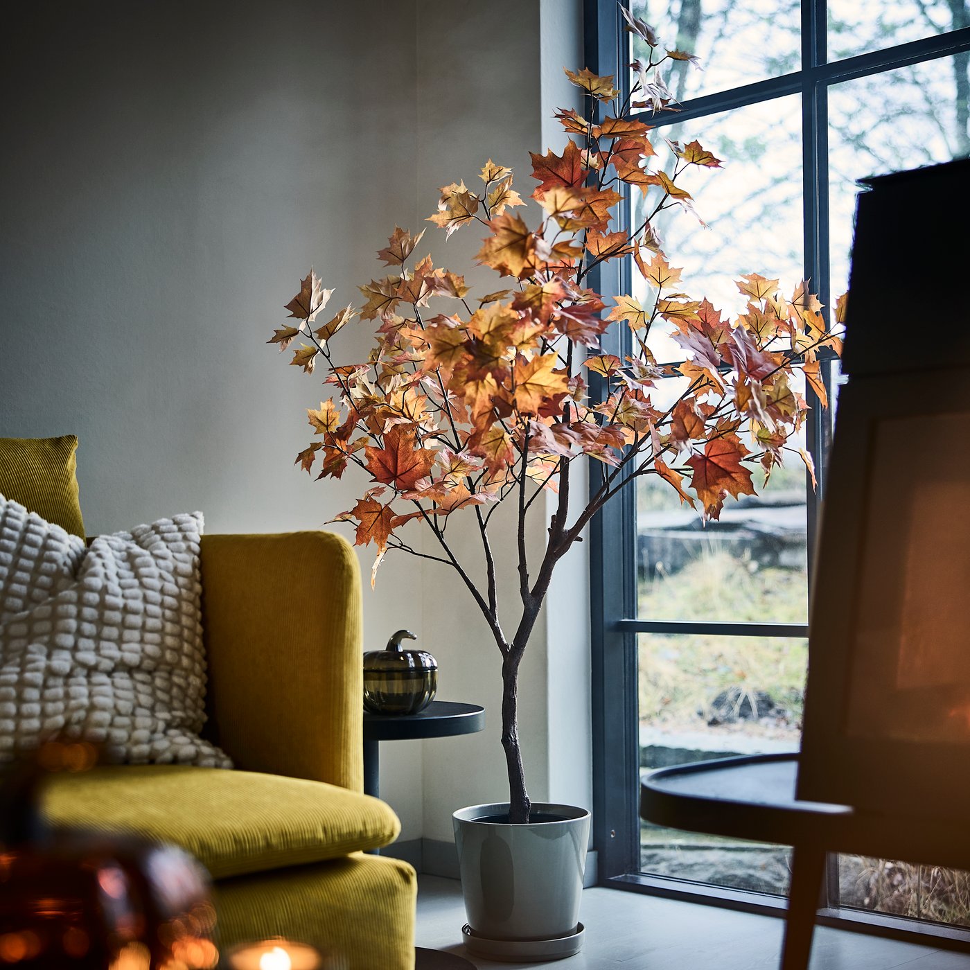 Un arce artificial FEJKA en una maceta, junto a un ventanal y un sillón.