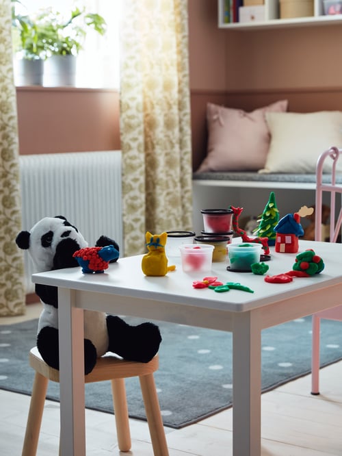 Children's room with multicoloured modelling dough cups on a table, and a soft toy panda bear on a children's stool.