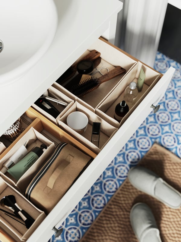 Armari de lavabo HEMNES blanc amb un calaix obert; dins del calaix hi ha uns organitzadors amb productes de bany.