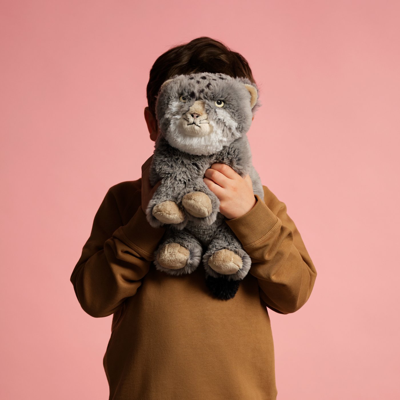 A child holding a grumpy-faced Pallas’s cat soft toy in front of their face.