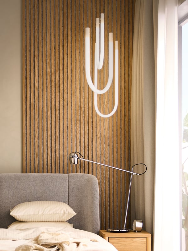 A TUFJORD double bed with storage with a VARMBLIXT LED pendant lamp hanging above it and a MODERMOLN work lamp by the side.