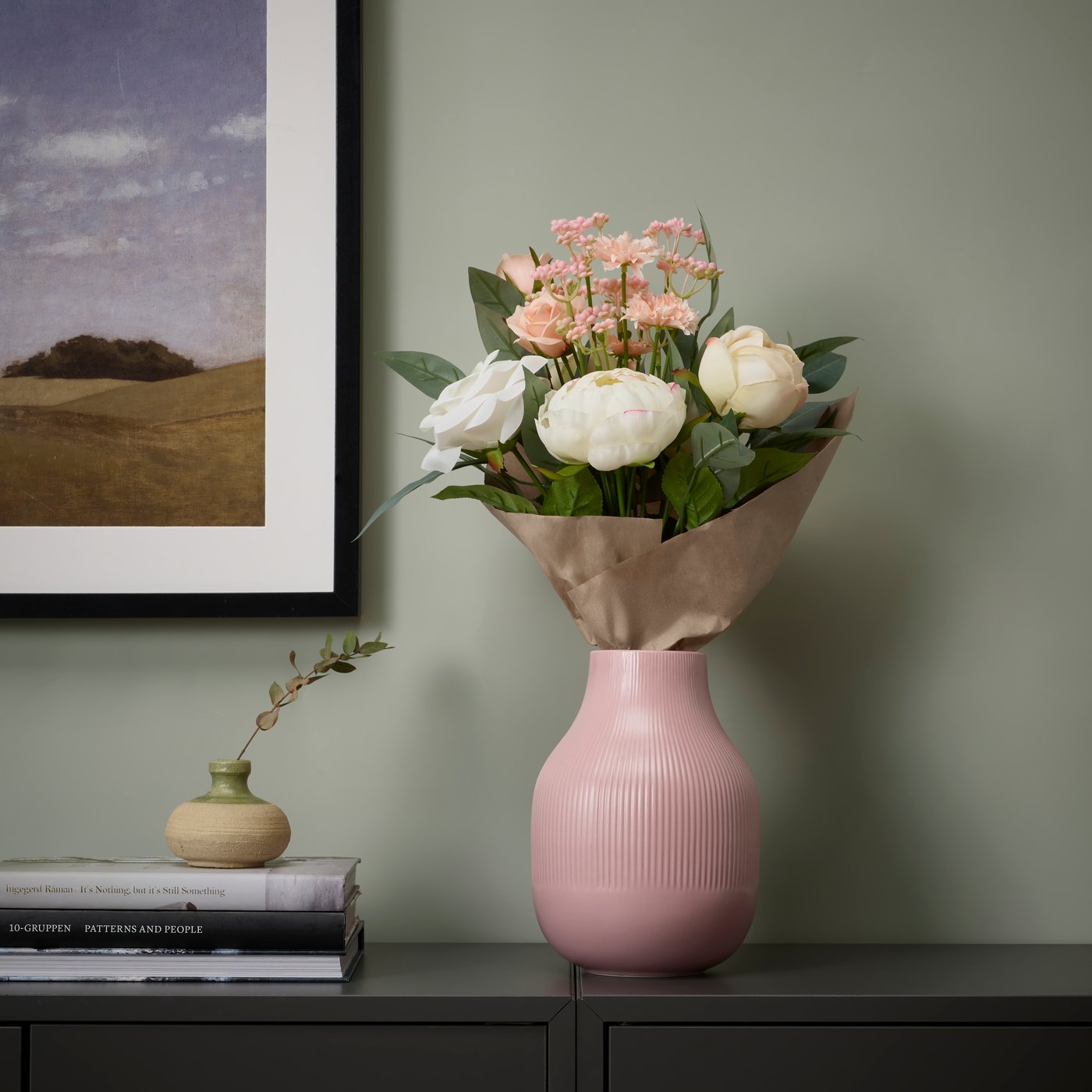 Tummalla tasolla on SMYCKA-tekokukkakimppu vaaleanpunaisessa GRADVIS-maljakossa.