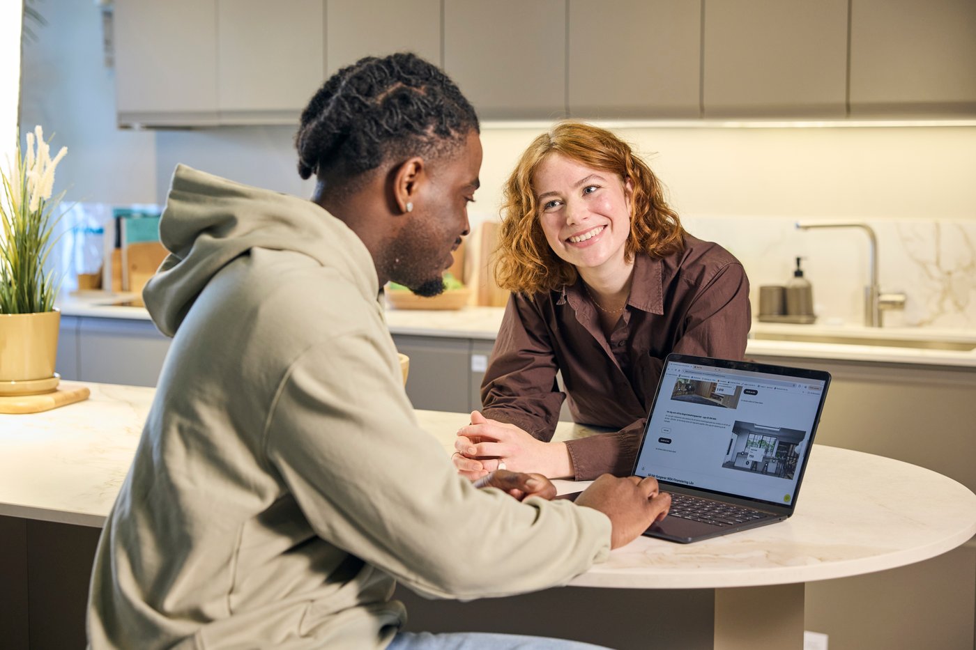A young couple looks at the laptop while sitting at their kitchen island.
