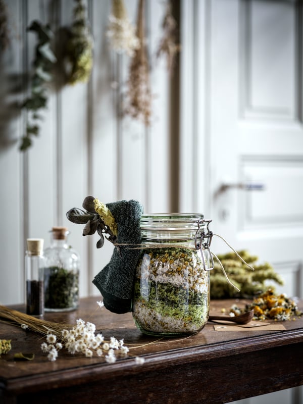 Un contenitore KORKEN con all'interno fiori per un tisana e con la decorazione HIMLEÅN. Accanto due contenitori IKEA 365+ su un tavolo di legno.