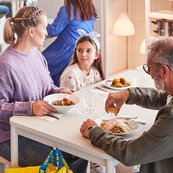 Two adults and a child about to enjoy a meal together while seated at a white table in an IKEA Swedish Restaurant.