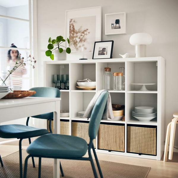Estante blanco KALLAX con 12 compartimientos, junto a una mesa de comedor.
