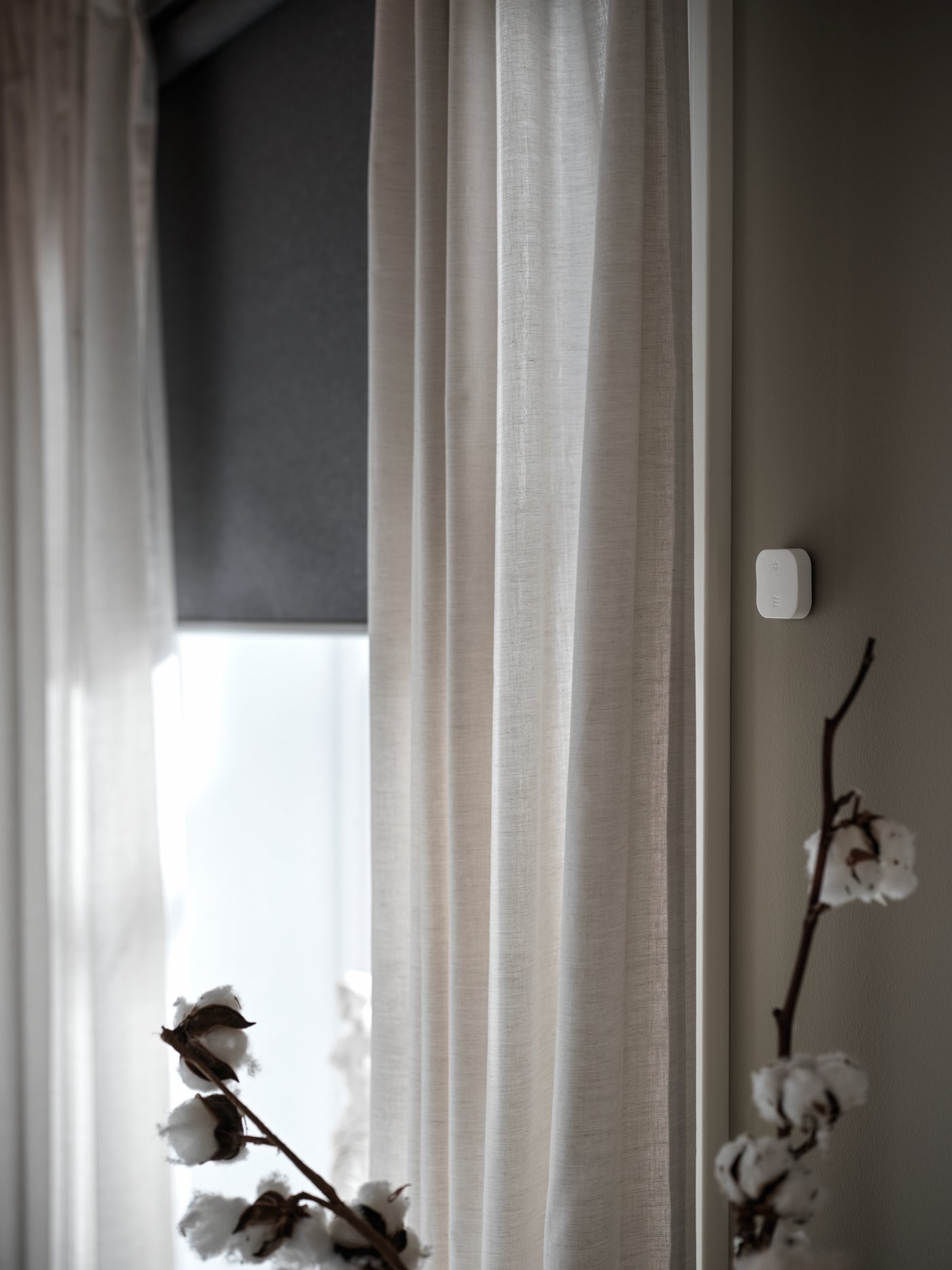 Ein schummrig erhelltes Zimmer mit halbtransparenten Gardinen am Fenster und einem halb geschlossenen FYRTUR Verdunklungsrollo.