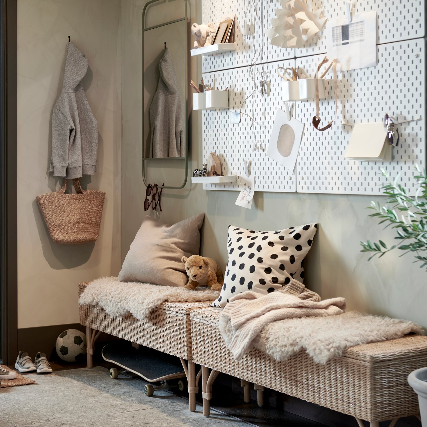 En hall med två rottingbänkar med förvaring inuti och kuddar och mattor ovanpå, samt vita förvaringstavlor och en grön spegel.