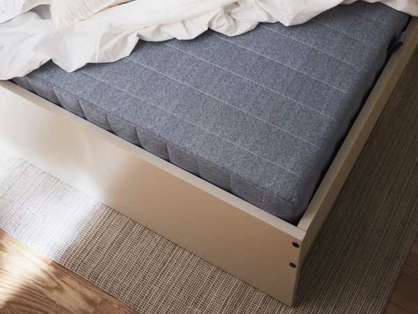 A corner of an extra firm/light blue VADSÖ sprung mattress on a GURSKEN bed with headboard.
