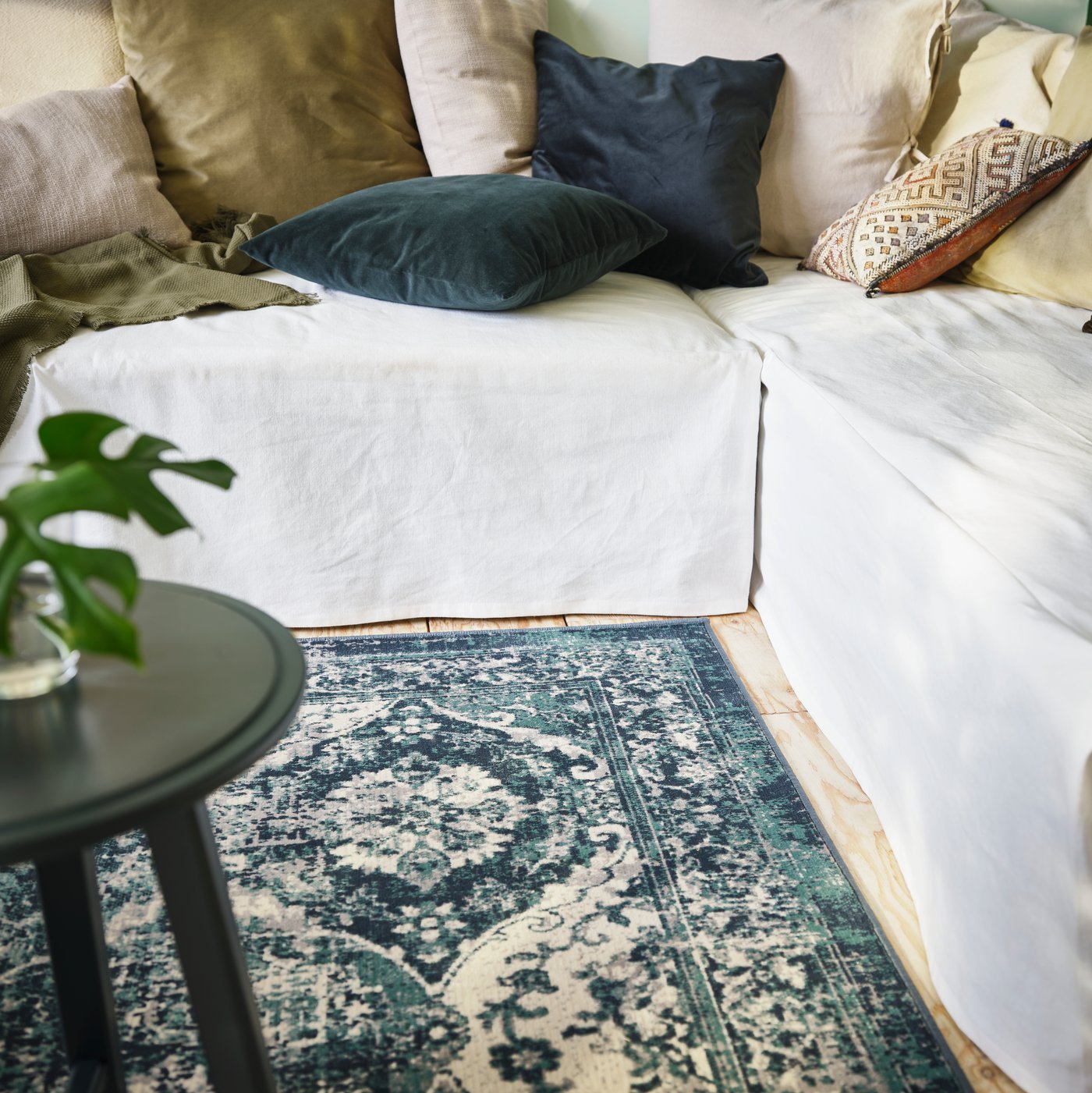 Alfombra de pelo corto VONSBÄK color verde, junto a un sofá con cojines de variados colores.