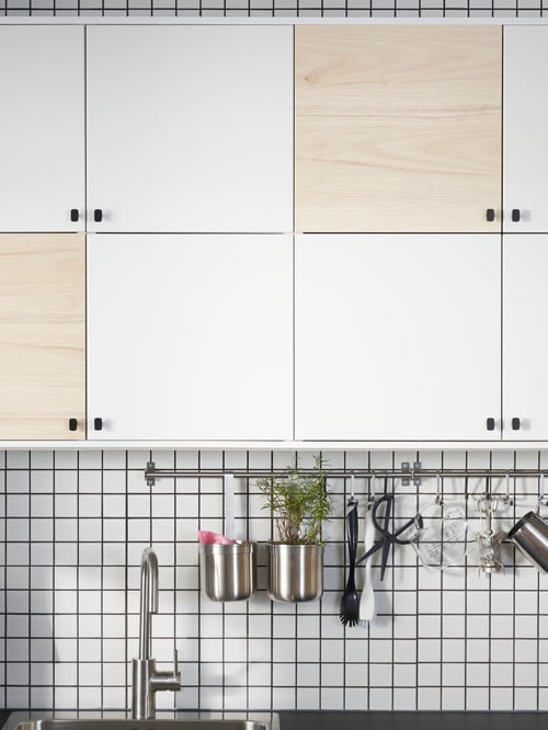 Küche mit METOD Wandschränken, die mit VEDDINGE Türen und HACKÅS Knöpfen versehen sind. Darunter ist vor einer weiß gefliesten Wand eine KUNGSFORS Stange mit KUNGSFORS S-Haken zu sehen, an denen KUNGSFORS Behälter und eine Schere befestigt sind. In die Arbeitsfläche ist eine Spüle mit einer ÄLMAREN Mischbatterie eingebaut.