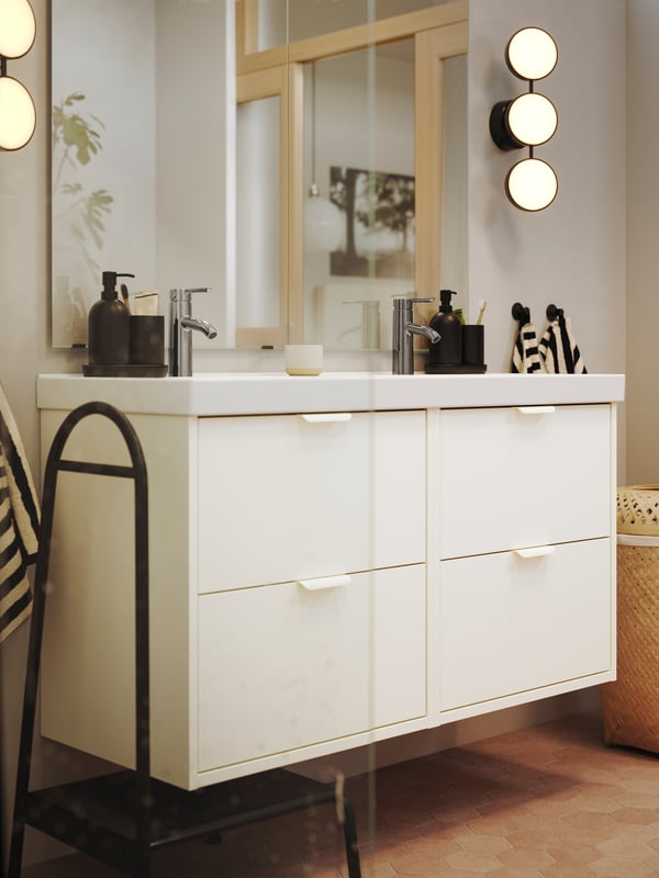 A bathroom has two white HAVBÄCK vanities with drawers and a double ORRSJÖN sink and a black KABOMBA wall lamp.