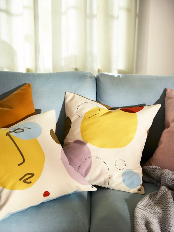 MANDELPIL and ÄNGSMÄTARE hand-embroidered cushion covers are on a pale blue sofa.