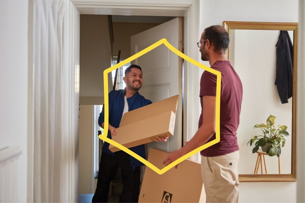 En mand i en lys entre modtager flade IKEA pakker fra en smilende leveringsmand.