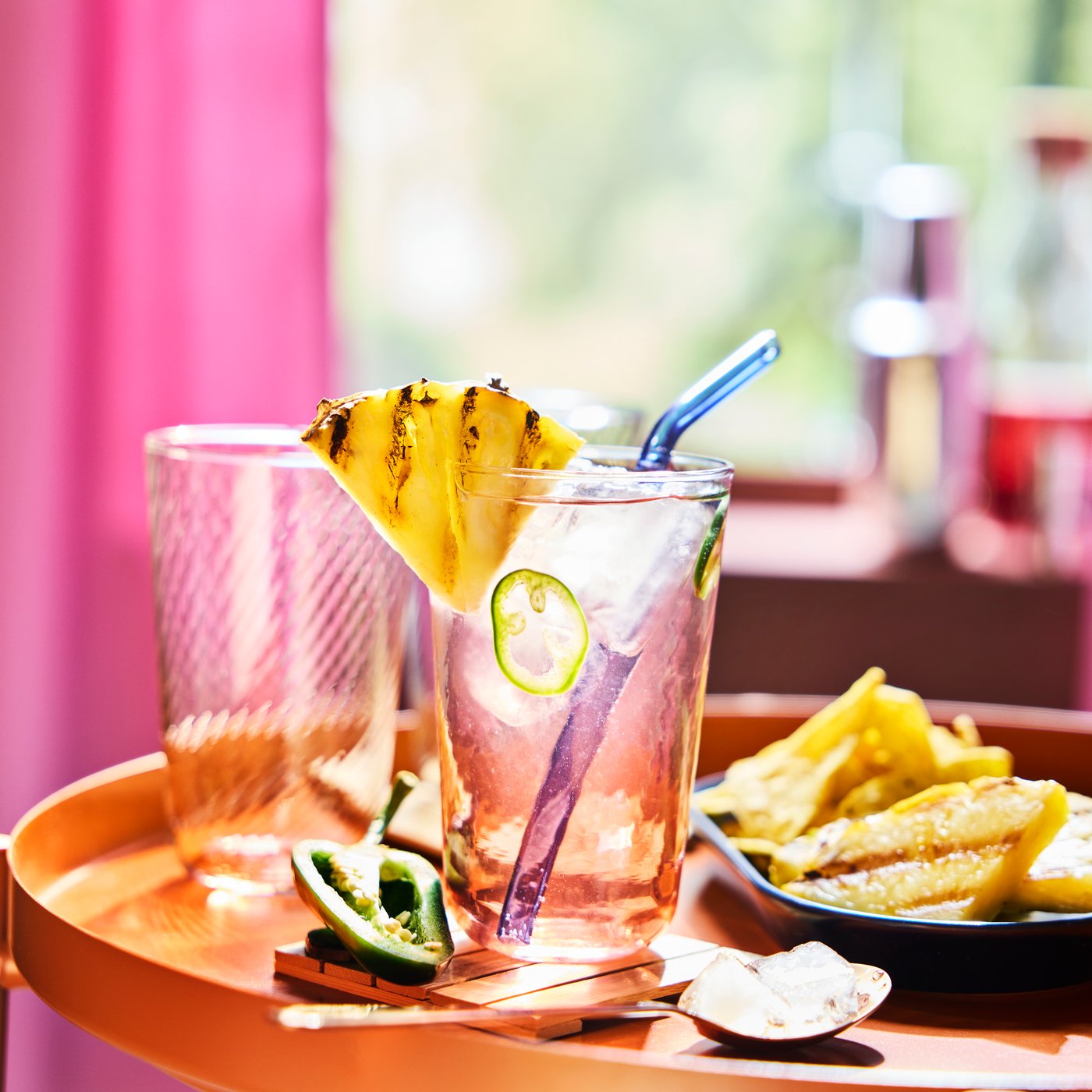 Ein gestreiftes rosa und klares KLIPPLAX-Glas mit Wellenmuster auf einem orangefarbenen Tisch, umgeben von mexikanischem Essen.