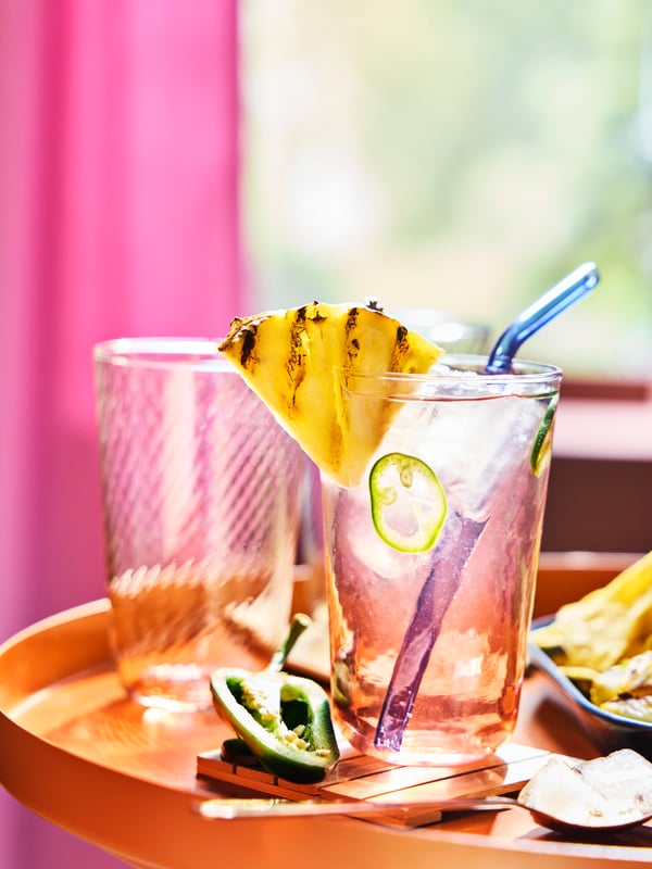 A striped pink and clear KLIPPLAX glass with ripple effect on an orange table surrounded by Mexican food.