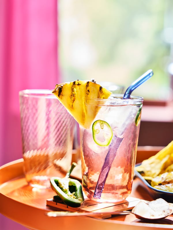 Un verre KLIPPLAX rayé rose et transparent avec effet d'ondulation sur une table orange entourée de nourriture mexicaine.