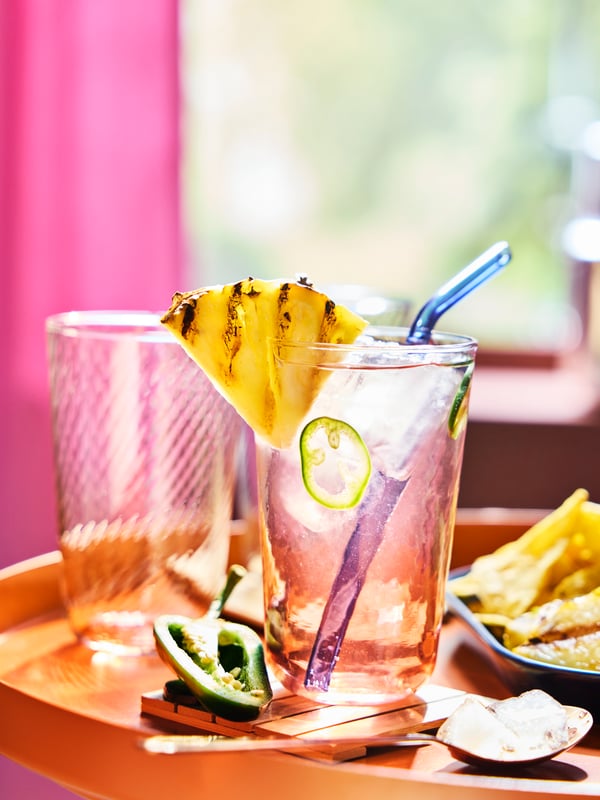 A striped pink and clear KLIPPLAX glass with ripple-effect on an orange table surrounded by Mexican food.