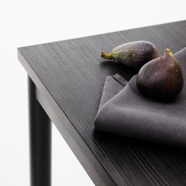 Close-up of the corner of a black SANDSBERG dining table. On top of the table, a black napkin and some figs.