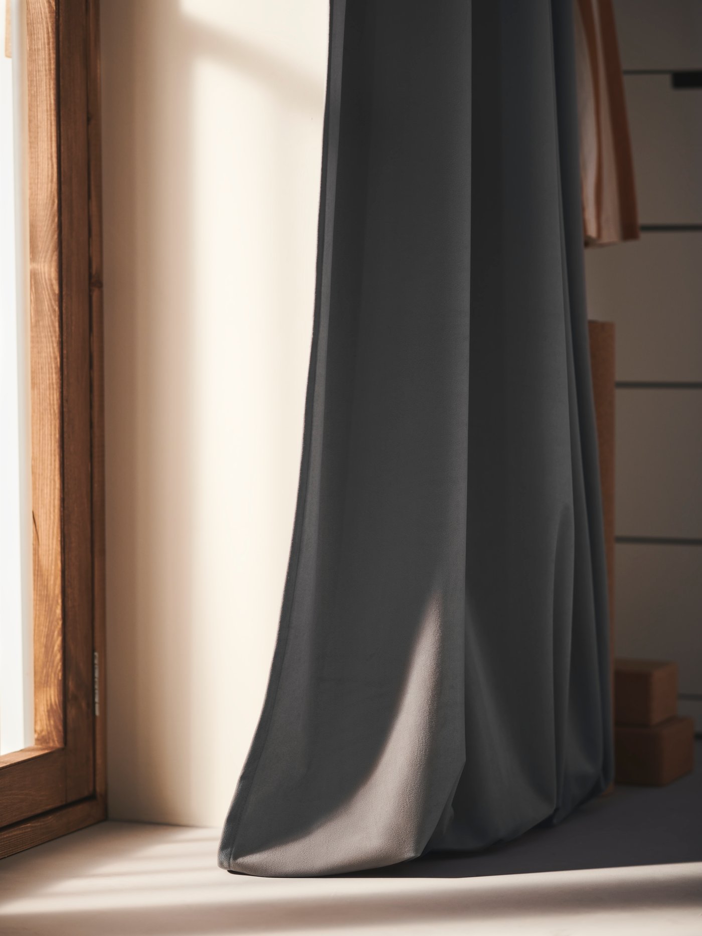 Солнечный свет струится через окно, сбоку которого висит занавеска САНДСВИНГЕЛЬ рядом с белым комодом НОРДЛИ с 7 ящиками.