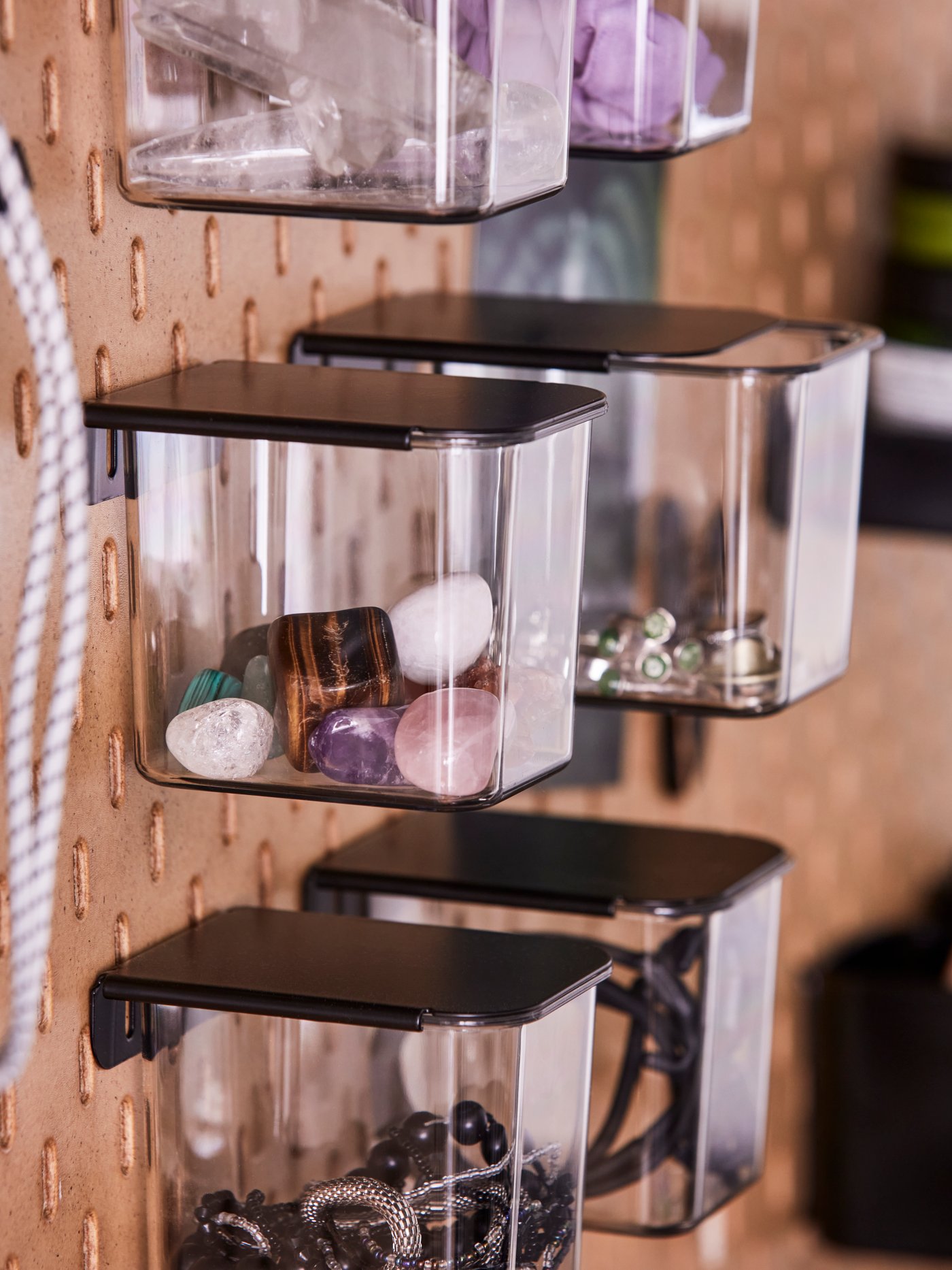 A close-up of six transparent and black SKÅDIS containers with lids with different things in them attached to a pegboard.