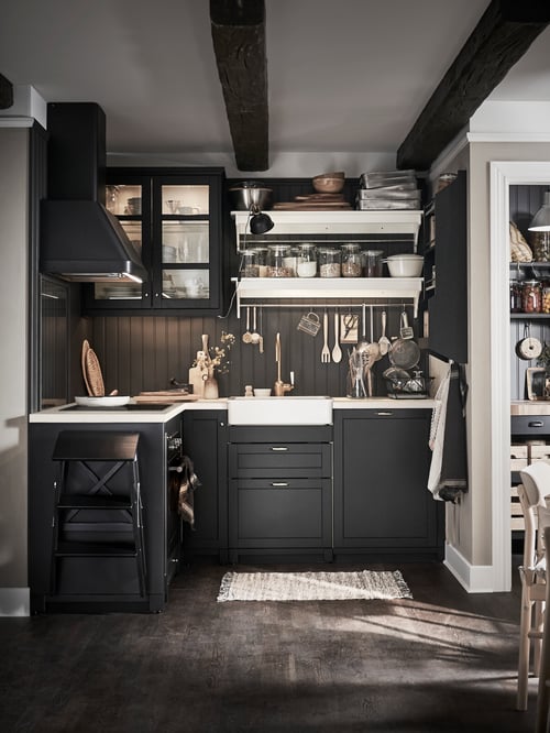 Kitchen with black base cabinets, wall cabinet, wall mounted extractor hood, hob, wall lamp, cooking utensils, dish drainer.