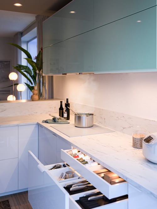 A modern kitchen with LED kitchen worktop lighting strip attached beneath wall cabinets with turquoise doors. 