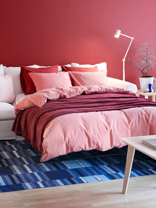 A white bed with headboard, brown patterned quilt cover and pillow cases, grey throw and cushions in white, grey and beige.
