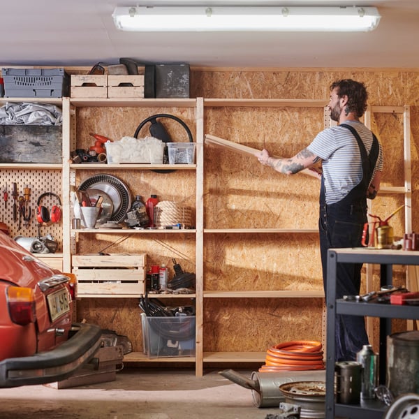 A person wearing overalls is adding a shelf to one of their IVAR shelving units in a garage.