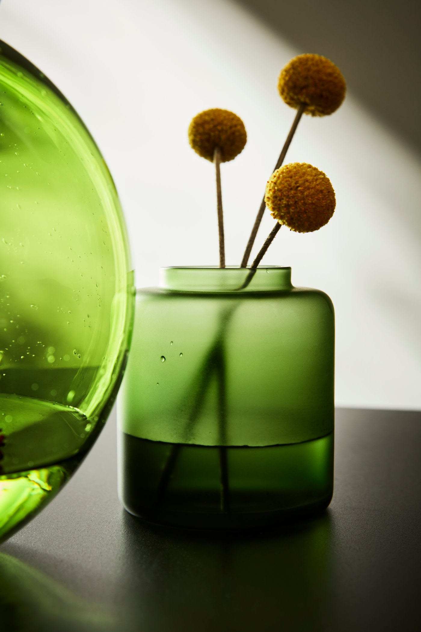 Närbild på en KONSTFULL vas i frostat grönt glas med tre kvistar i.