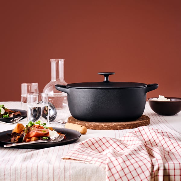 A VARDAGEN casserole with lid on a HEAT pot stand in dark brown and DRAGON cutlery in stainless steel, a plate and glasses.