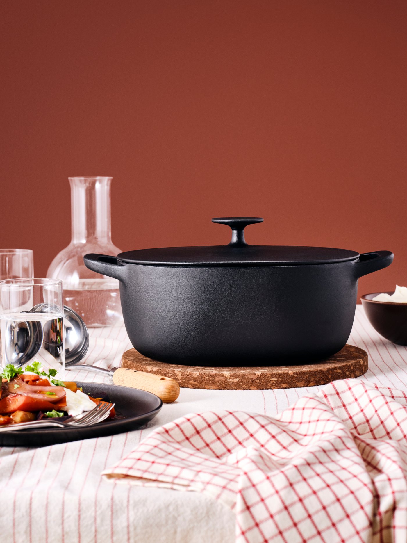 A VARDAGEN casserole with lid on a HEAT pot stand in dark brown and DRAGON cutlery in stainless steel, a plate and glasses.